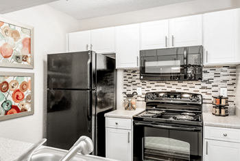 A black refrigerator stands in a kitchen with white cabinets and a black stove.